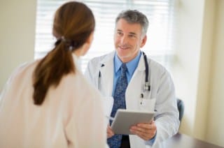 Happy male doctor with digital tablet discussing with female colleague in clinic