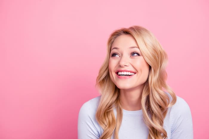 Portrait with empty place of foolish childish funny girl with modern hairdo beaming smile looking at copy space laughing isolated on pink background