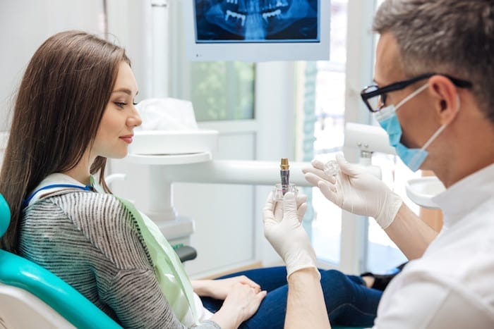 Male dentist showing his female patient a dental implant in clinic
