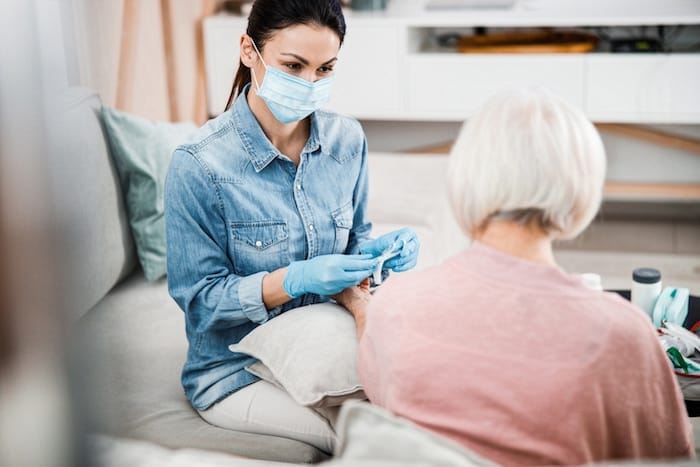 Physician in medical face mask holding syringe while senior lady keeping arm on cushion stock photo