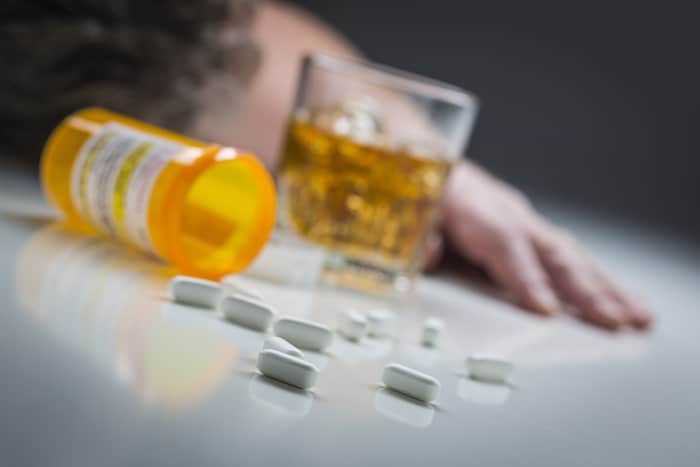 Unconscious Man Face Down Behind Scattered Prescription Drugs and Glass of Alcohol.