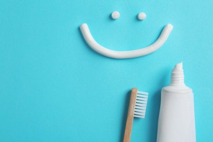 Smiling face made of toothpaste, tube, brush and space for text on color background, top view