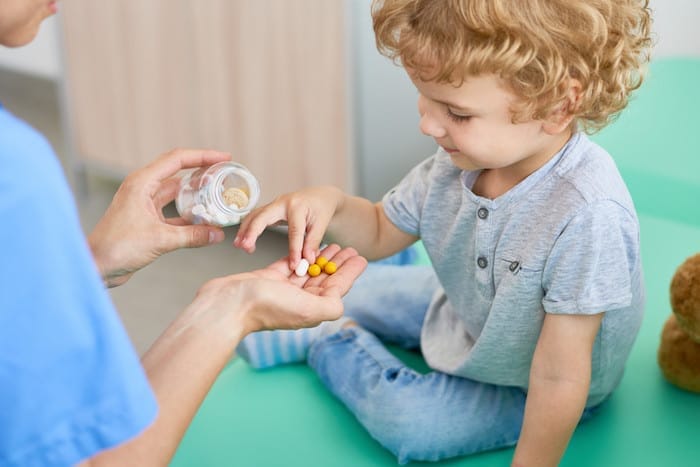 Unrecognizable pediatrician giving vitamins to curly little patient after completion of check-up, blurred background