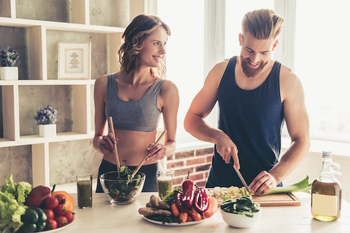 Beautiful young sports people are talking and smiling while cooking healthy food in kitchen at home