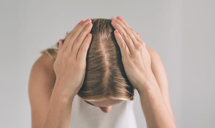 Women's hair is a top view close-up. Blonde woman is wearing shirt isolated on white.