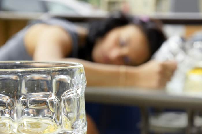 Alcohol abuse: drunk young woman or student lying down on a table with beer bock still in hand, focus on glass up front.