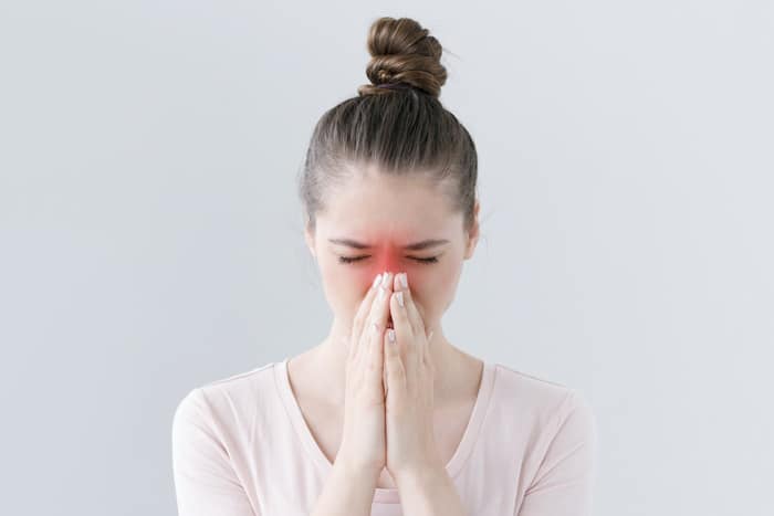 Closeup of young European female isolated on gray background looking stressed, putting hands together as if she is praying with closed eyes to overcome depression and find solution to problem.