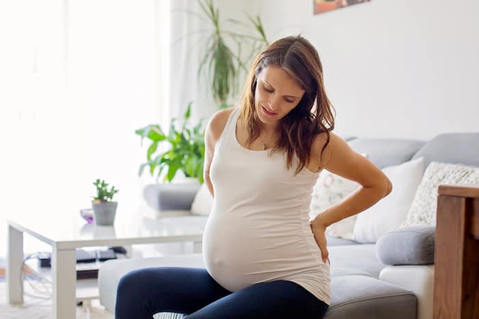 Young pregnant woman, having painful contraction, starting labor, sitting on the couch
