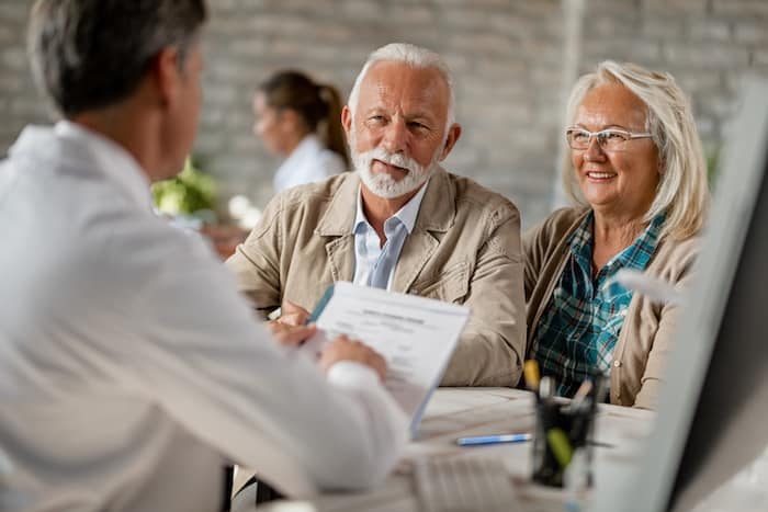 Happy mature couple informing themselves about health insurance while talking to a doctor at clinic.