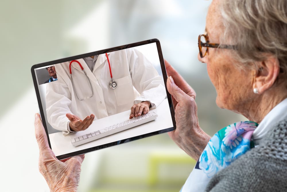 Mature adult women consults a e-health doctor with tablet computer sitting in soft chair. In touchscreen, male doctor