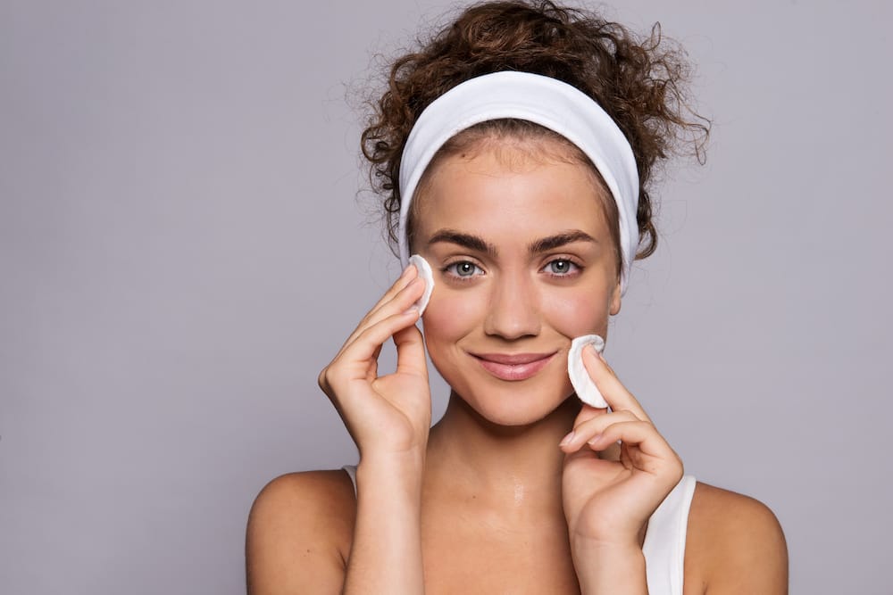 A portrait of a young woman cleaning face in a studio, beauty and skin care.