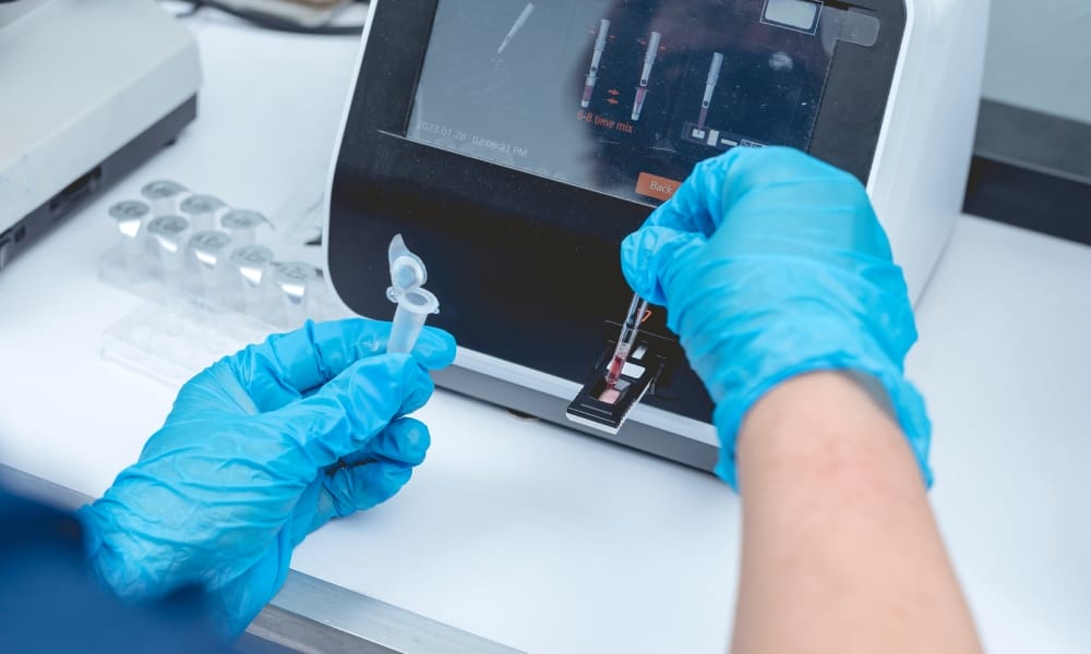 A doctor putting a sample into a testing machine to learn about its composition. They are handling the sample with gloves.