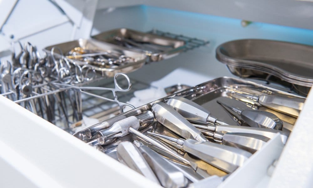 A storage container full of medical instruments used for surgery. These instruments include forceps, drills, and trays.