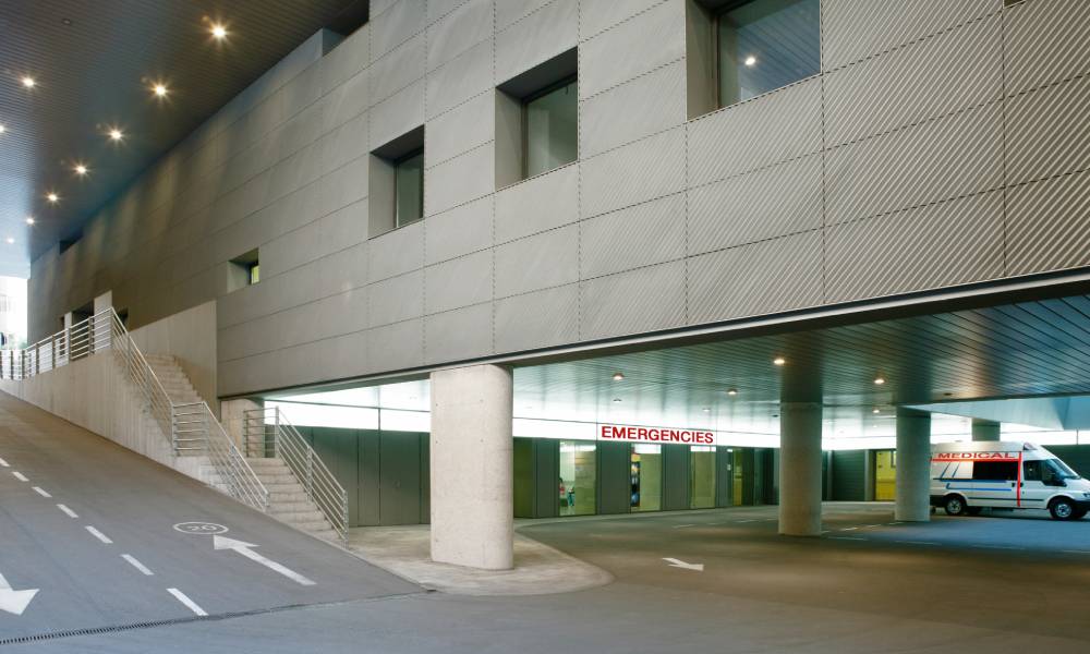 An underground hospital parking lot with an entrance that reads "EMERGENCIES." An ambulance is parked nearby.