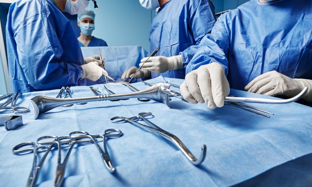 An operating room with surgeons and techs gathered around a surgical instrument tray. They're in scrubs and gloves.