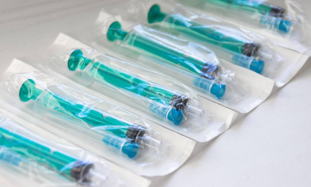 A line of plastic turquoise syringes with a needle in a plastic tube with a blue cap sit inside clear packaging.