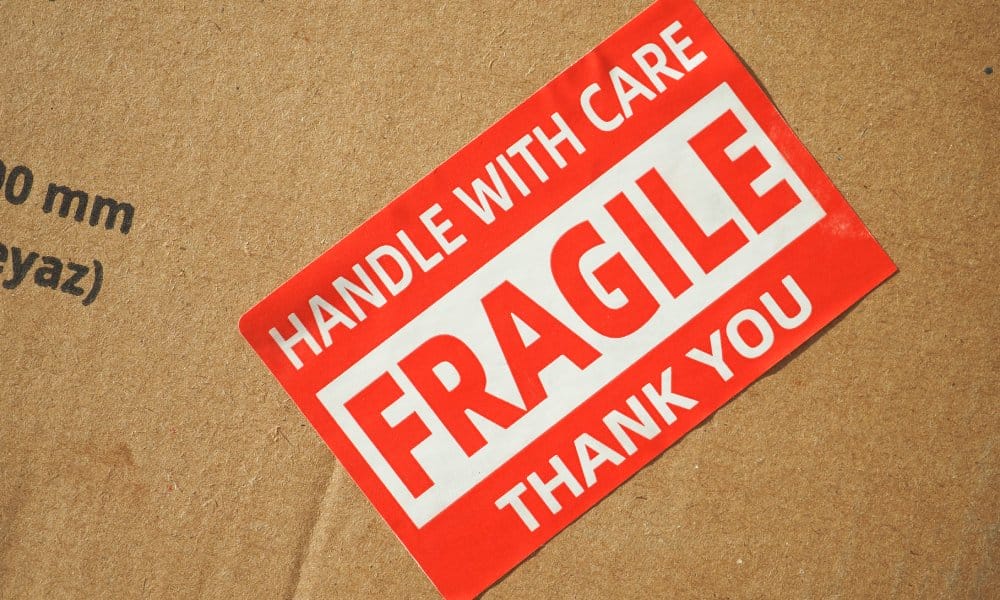 A red and white sticker on a cardboard shipping box that reads "Fragile: Handle With Care: Thank You."