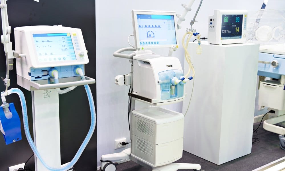 Three pieces of bulky white medical equipment are propped up in front of a wall in a healthcare facility.