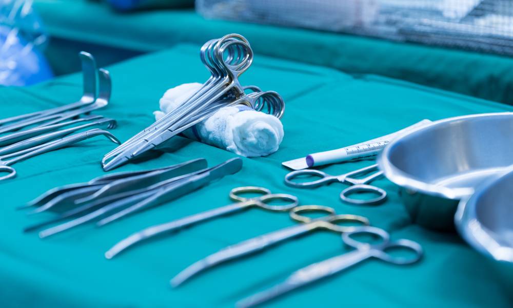 Metal surgical clamps, tweezers, and other medical equipment sit on on a table with a green tablecloth.