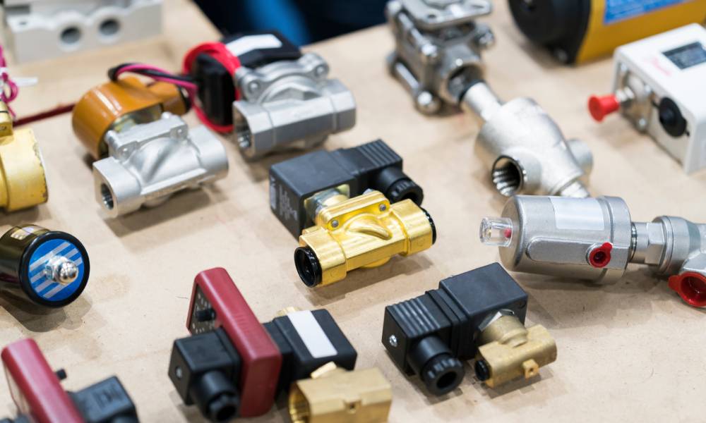 A collection of eleven different types of solenoid valves laid out on a sheet of pressboard.