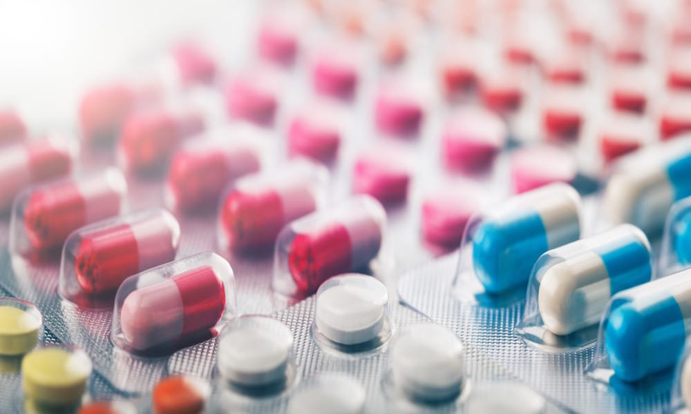 A close-up of a heap of medical pills and tablets of various colors, like white, blue, and red, in transparent packaging.