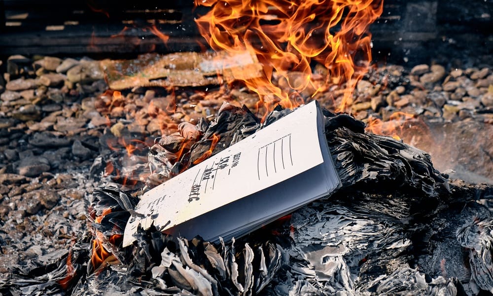 A close up of a burn pile with flames in the back and a stack of medical documents in the front getting ready to burn.