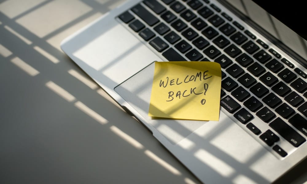 A yellow sticky note attached to a silver and white laptop computer keyboard that reads "welcome back!"