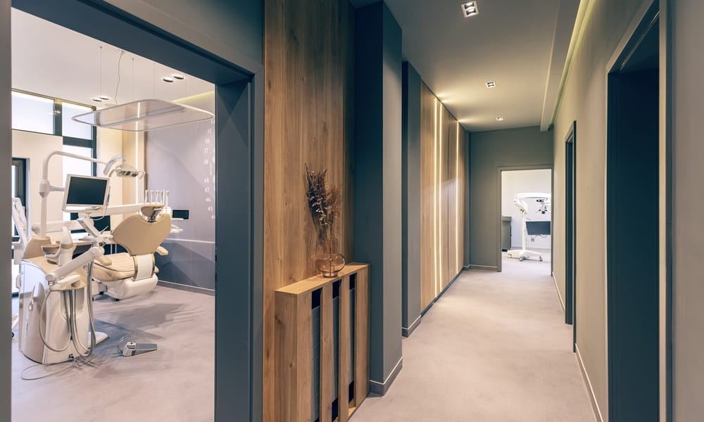 The hallway of a modern dental office features a wooden accent wall and a view into a patient exam room.