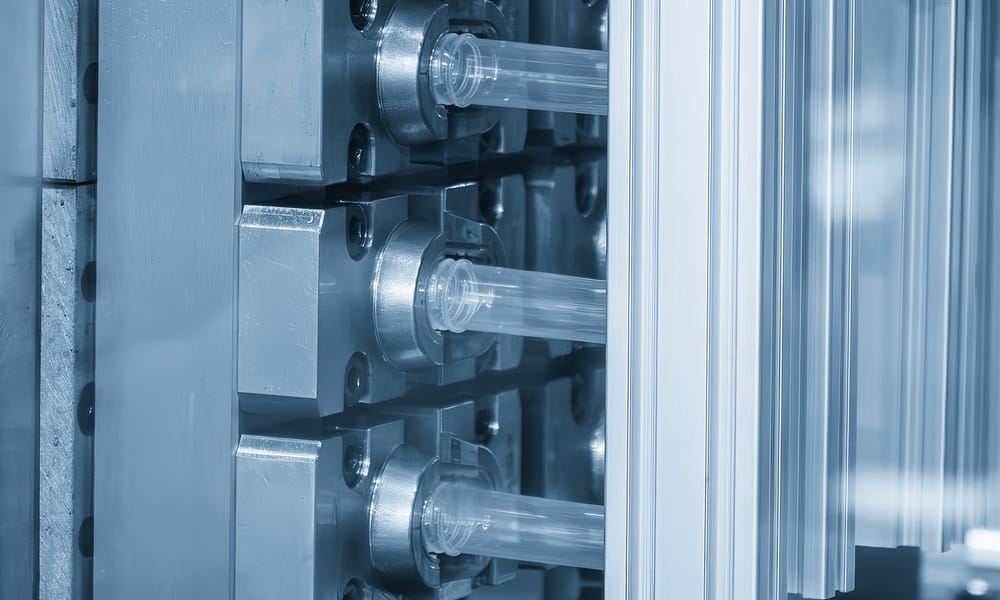 A close-up of three newly made medical plastic tubes in a plastic injection molding machine.