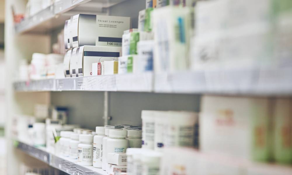 A close-up of several shelves in a pharmacy containing various medication bottles and boxes lined up together.
