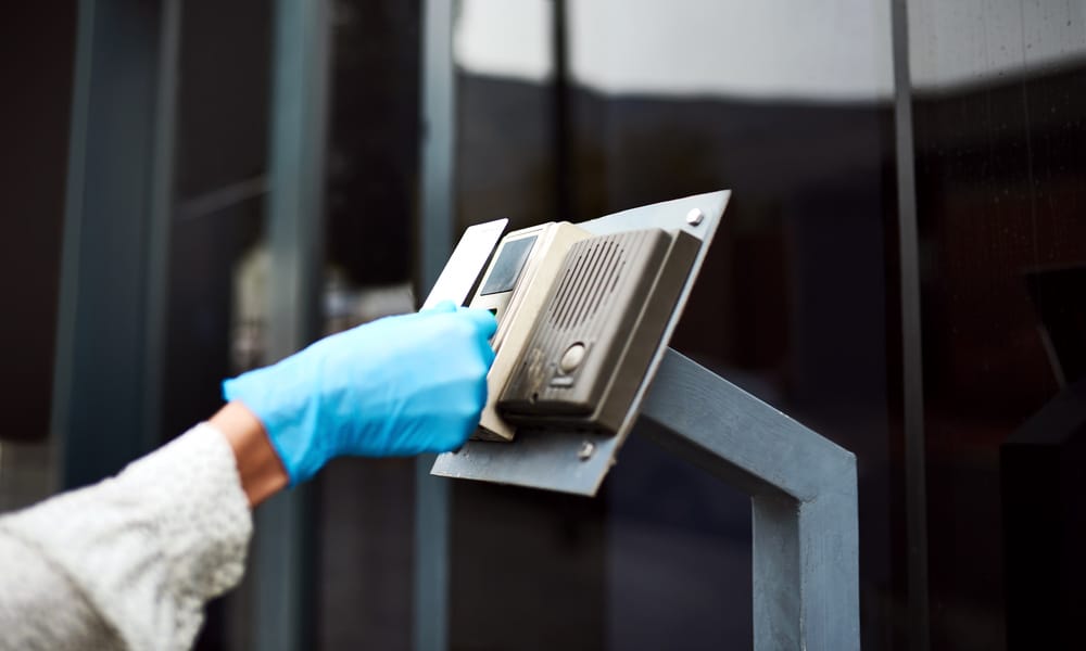 A healthcare worker wearing blue latex gloves as they hold a keycard up to the entry scanner. They're wearing a white coat.