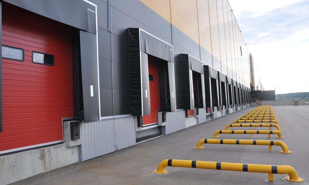 The backside of a hospital with multiple overhead doors for entry. The doors are red with yellow barricades.