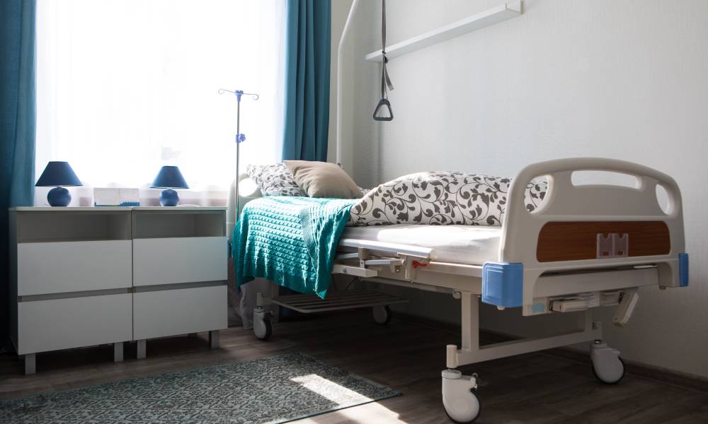 A home hospital bed with blankets and a mobility pull-handle sits in the corner of a room next to two dressers.