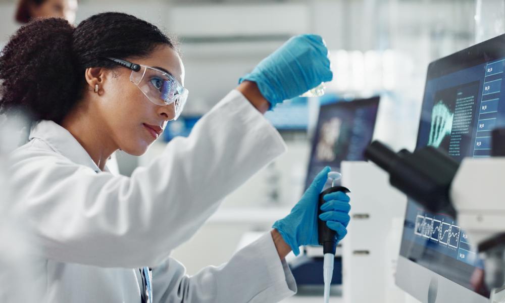 A woman is in a scientific lab, wearing a white coat, and is concentrating on the test beaker in her hand.