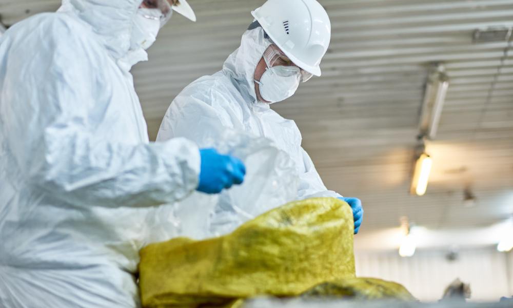 Two workers wearing white biohazard suits are working at a waste processing plant and are sorting items.