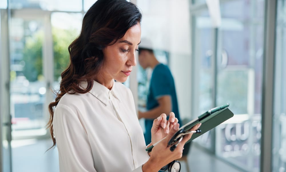 A professional woman medical administrator is typing something on their touchscreen tablet in the medical office.