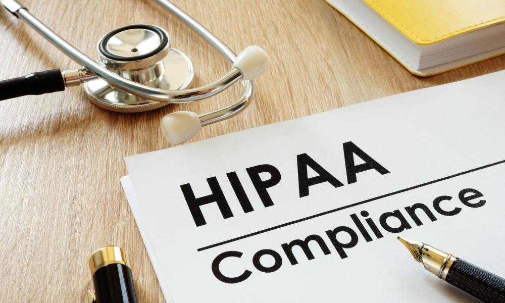 A close-up of a HIPAA compliance document on a light brown wooden desk next to a notebook, pen, and stethoscope.