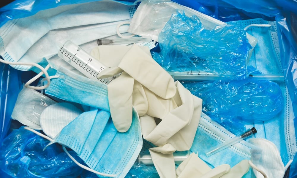 A close-up of a medical bin full of used face masks, needles, sterile gloves, and medical supply plastics.