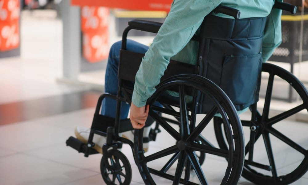 The lower half of a person's body sitting in a wheelchair. The person's hands are on the chair's wheels.